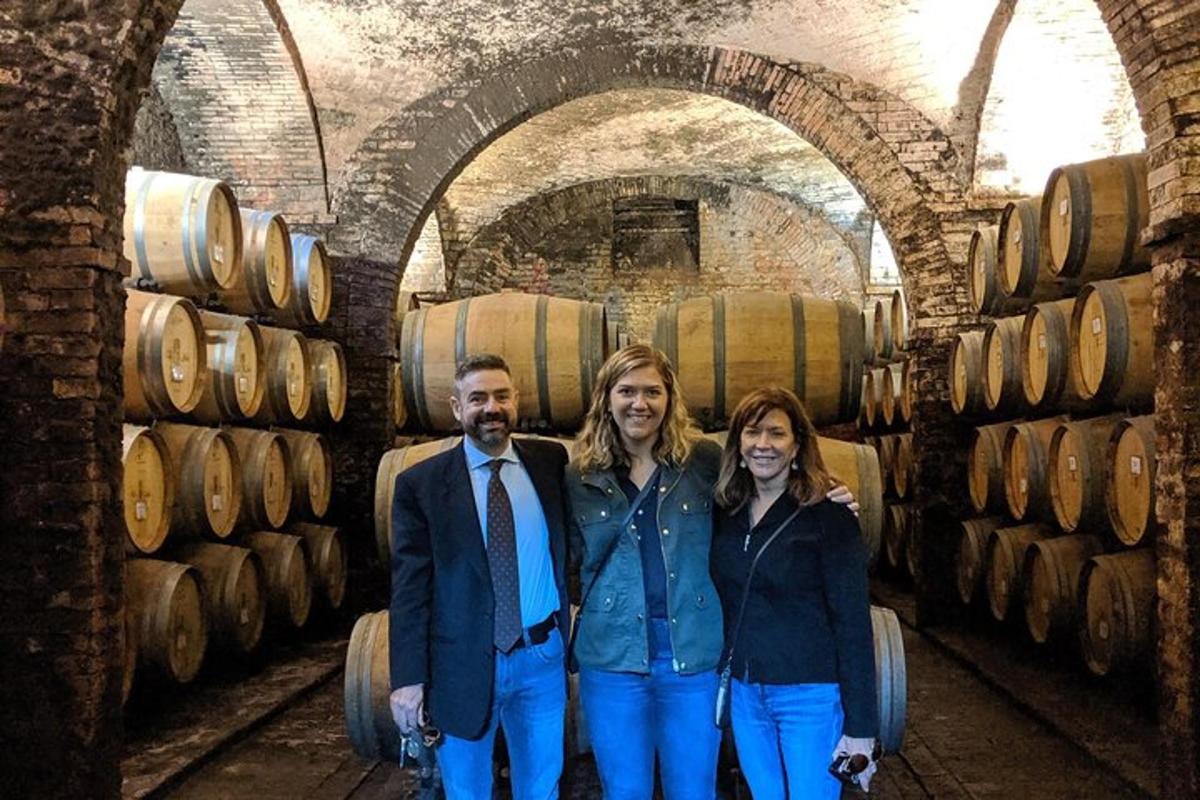 troje ljudi stoje ispred bačvi u vinariji