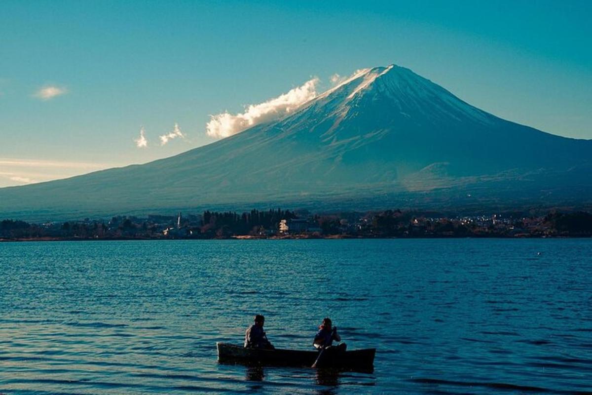 two people sitting in a boat in the water with a mountain
