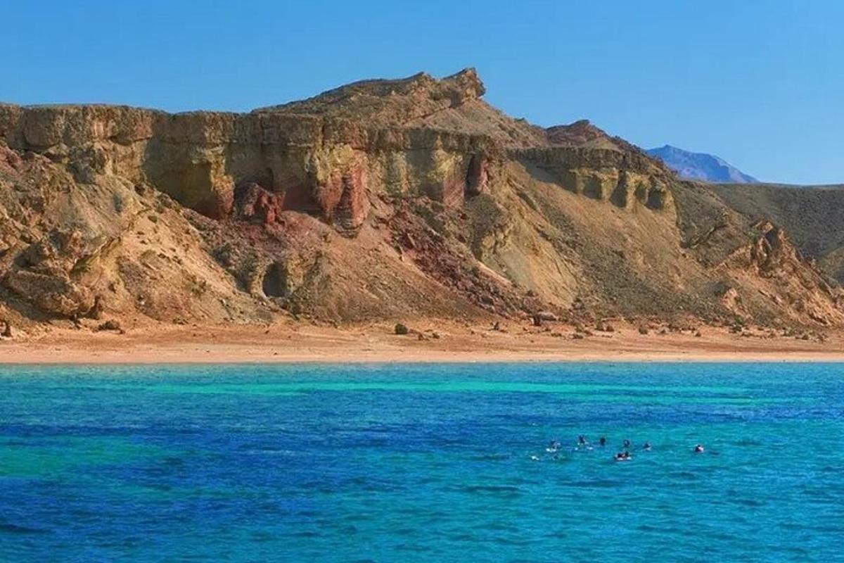 un grup de persones nedant a l'oceà prop d'una muntanya