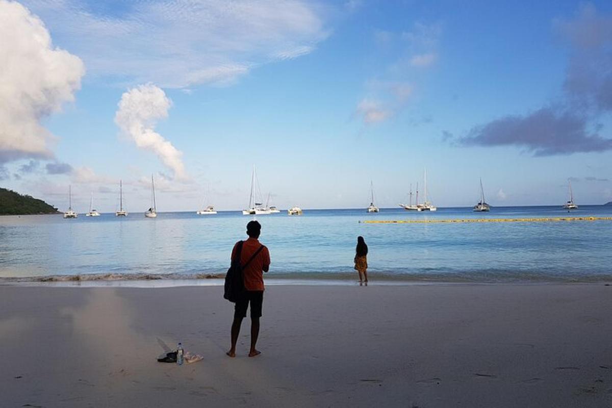 two people standing on the beach looking at the water