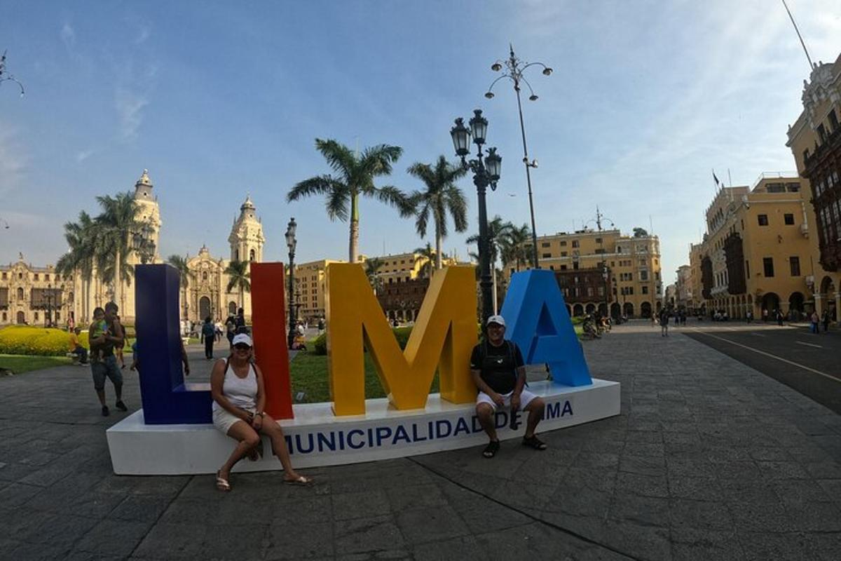 Dos personas sentadas frente a un cartel en una ciudad.