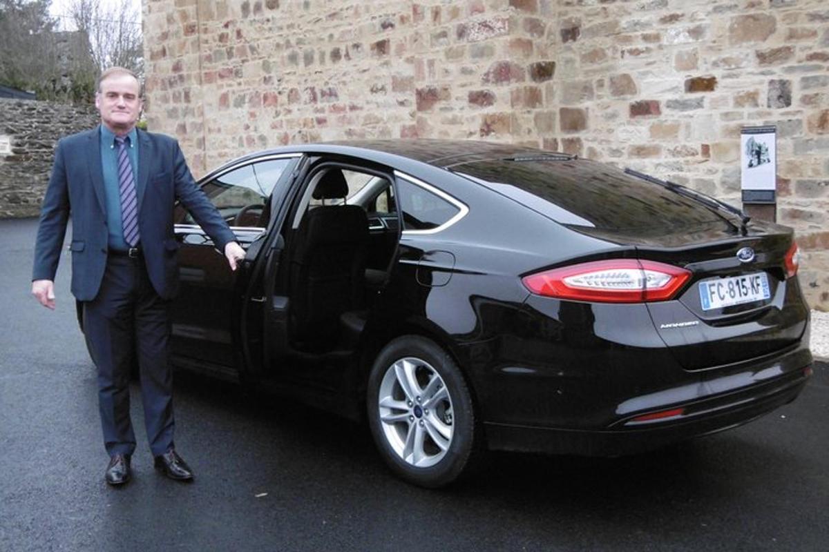 a man in a suit standing next to a black car