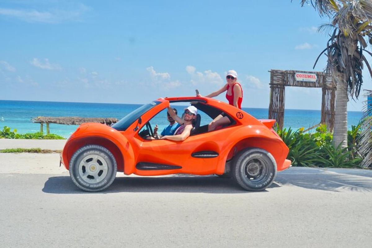 duas pessoas em um pequeno carro laranja na praia