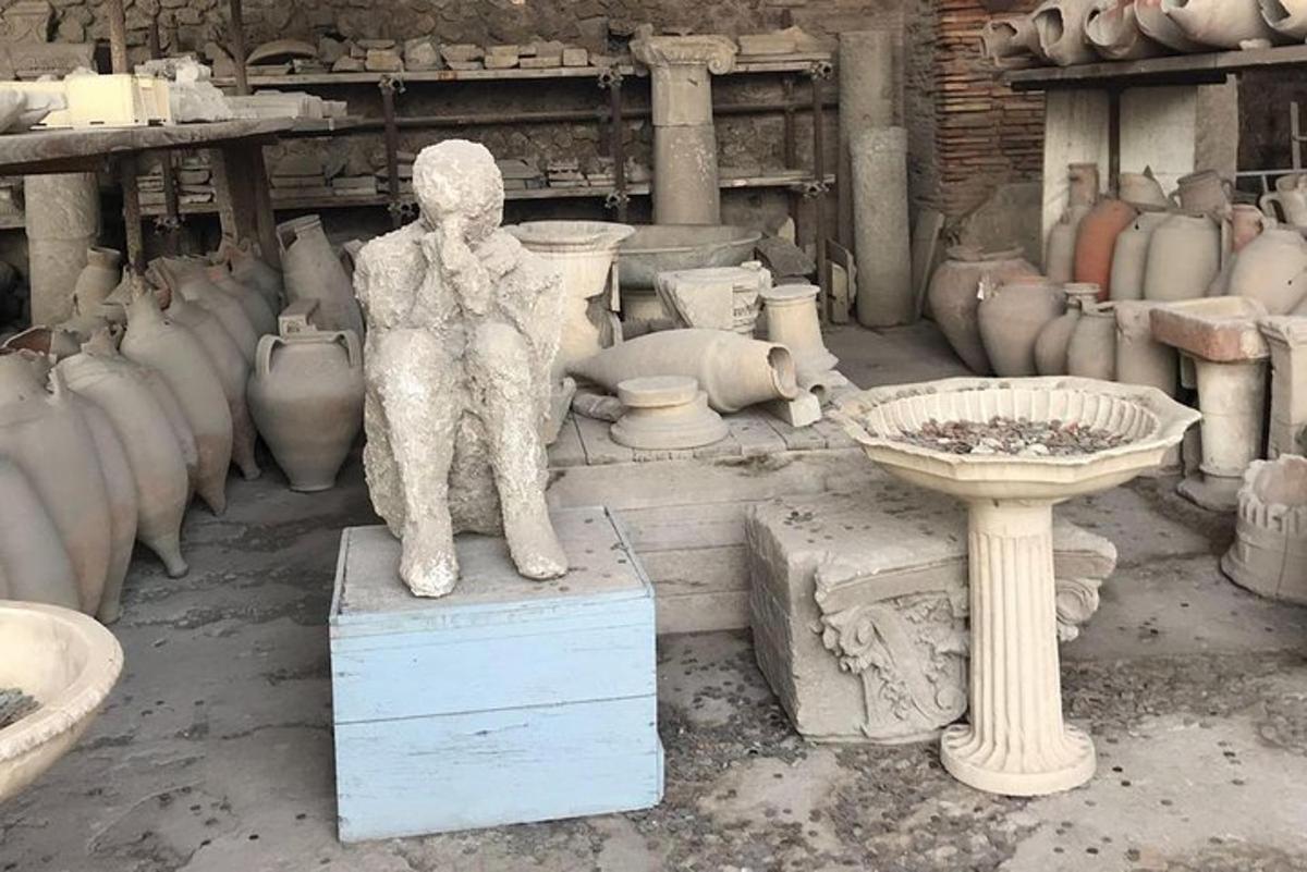 una statua di una persona in piedi su una scatola in una stanza con dei vasi