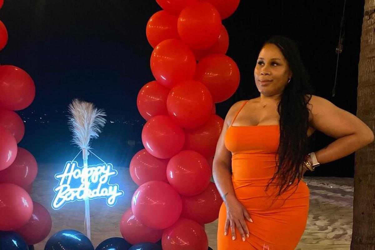 seorang wanita berpakaian oren berdiri di sebelah sekumpulan belon