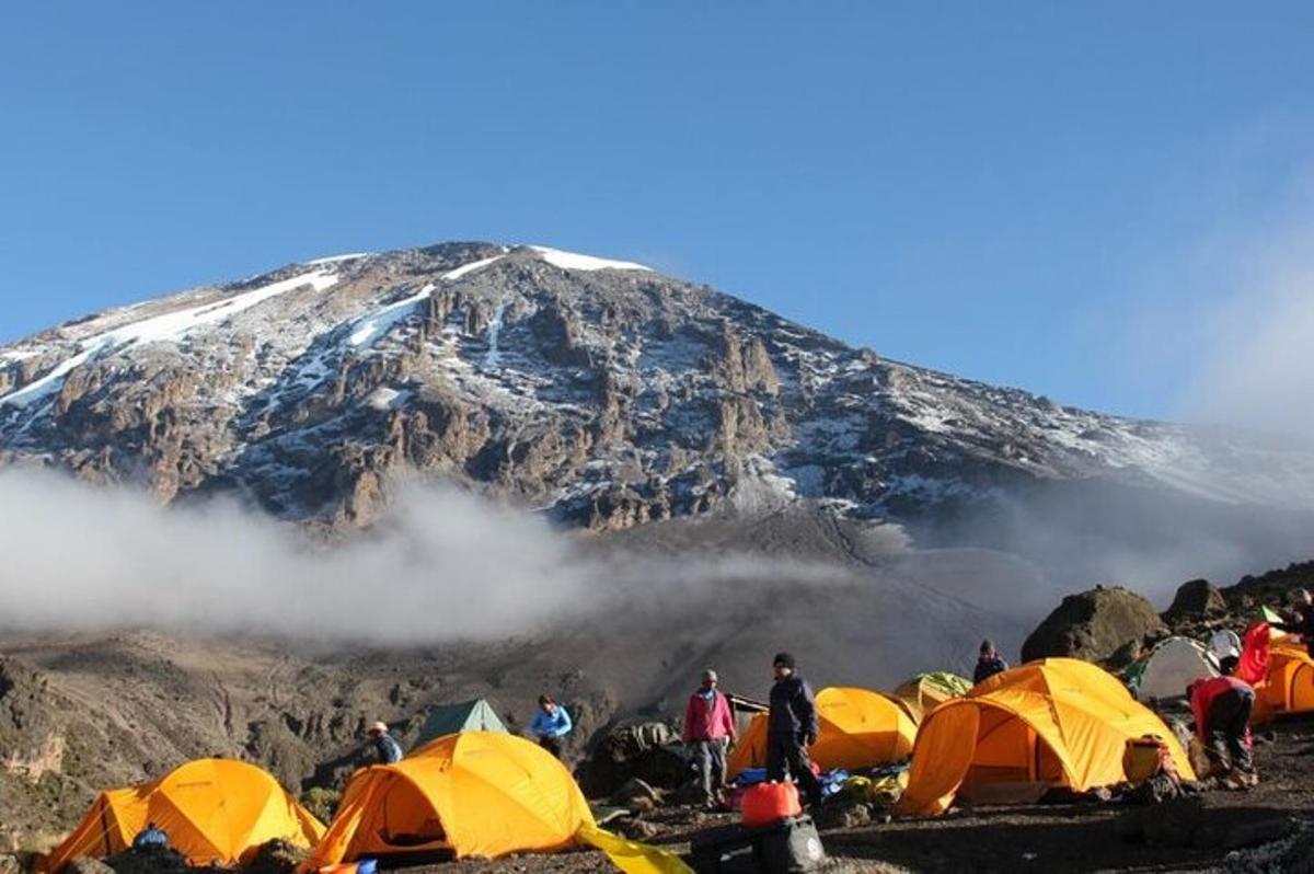 hópur fólks stendur í kringum tjald fyrir framan fjall