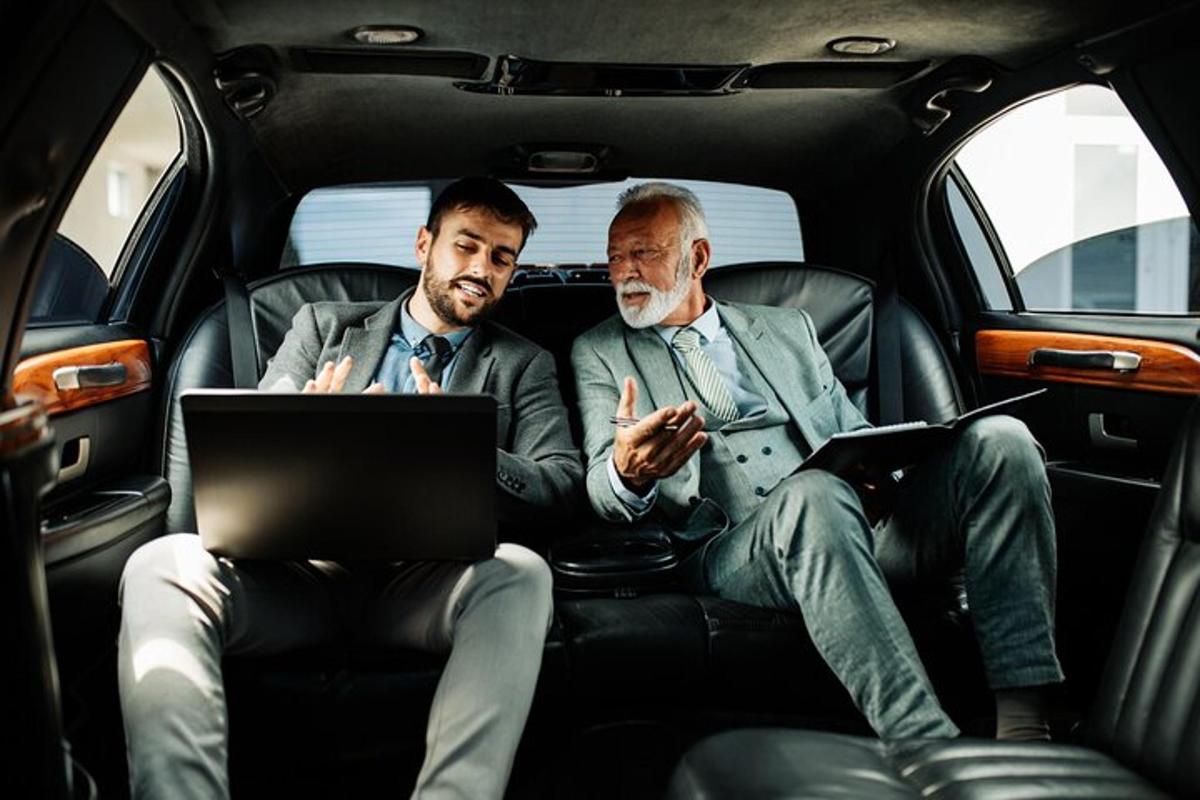 due uomini seduti sul sedile posteriore di un'auto con un computer portatile