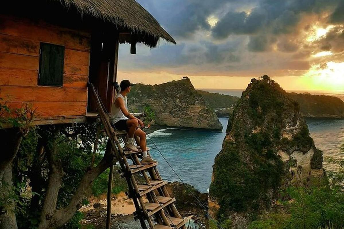 seorang lelaki duduk di atas tangga di luar rumah yang menghadap ke lautan