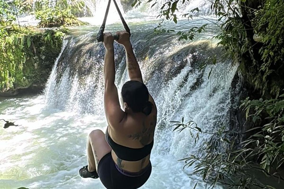 een vrouw in bikini hangt aan een touw boven een waterval