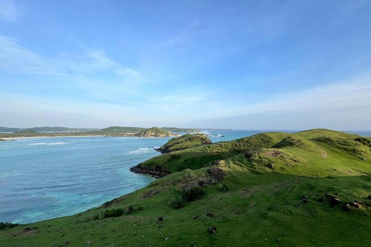 a green hill next to the ocean with the ocean