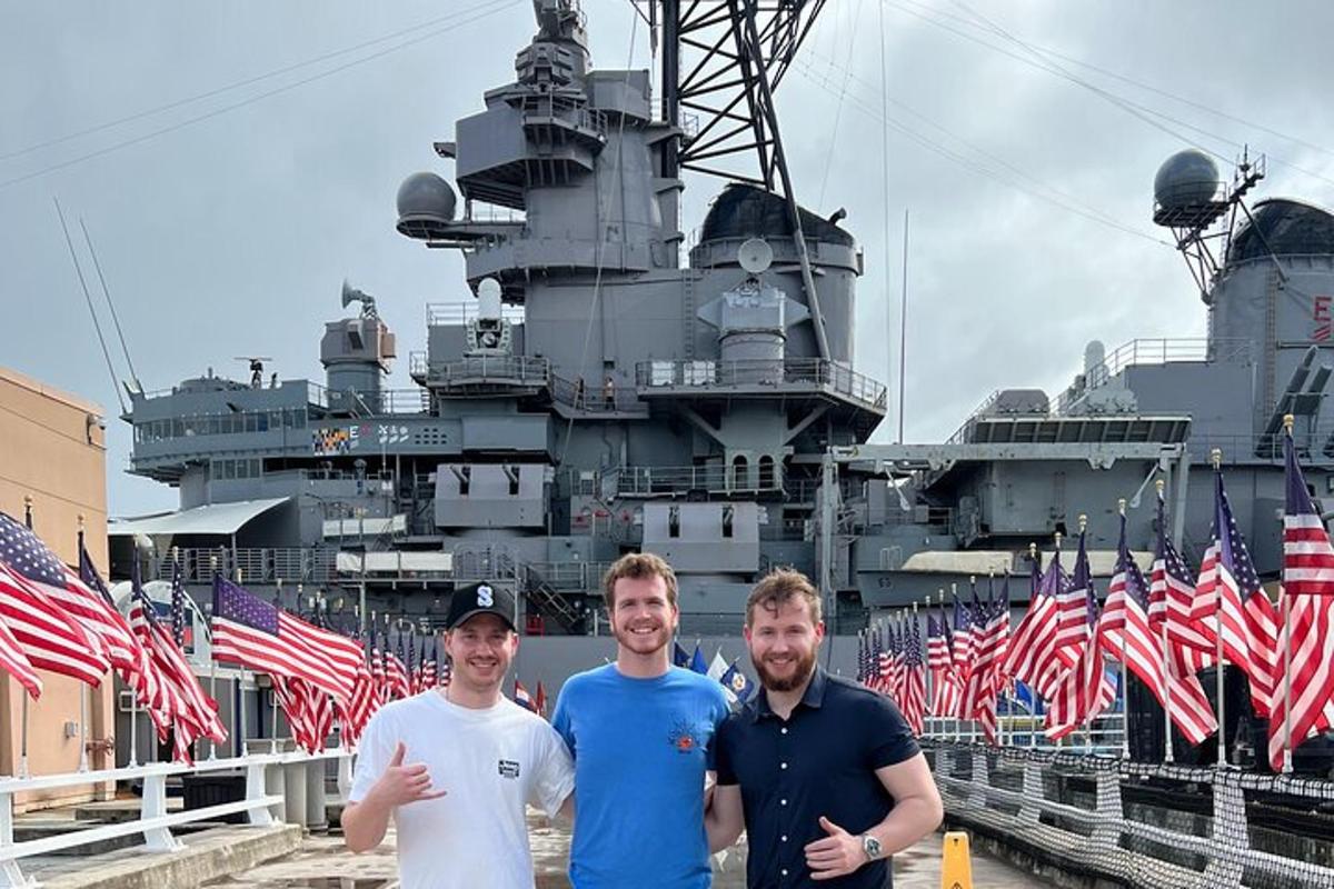 trois hommes debout devant un cuirassé avec des drapeaux américains
