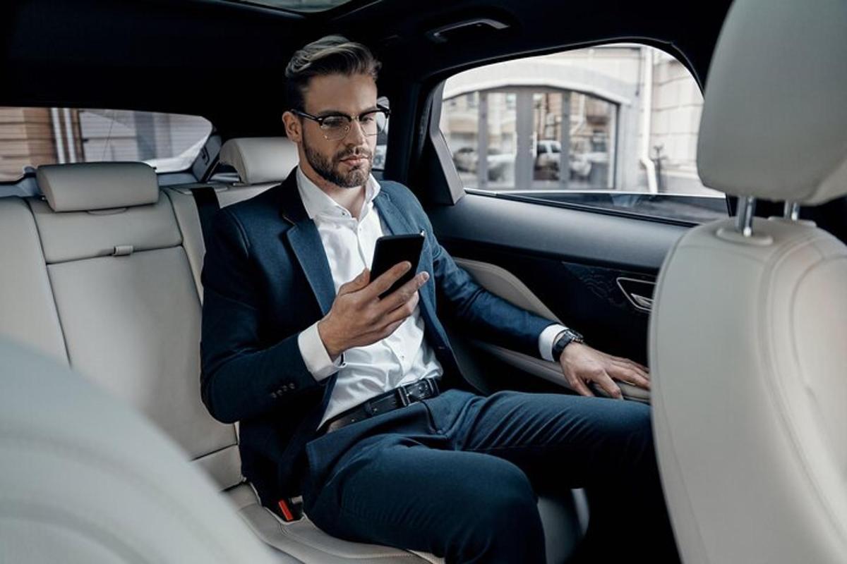 egy férfi ül egy autó hátsó ülésén, és a mobiltelefonját nézi