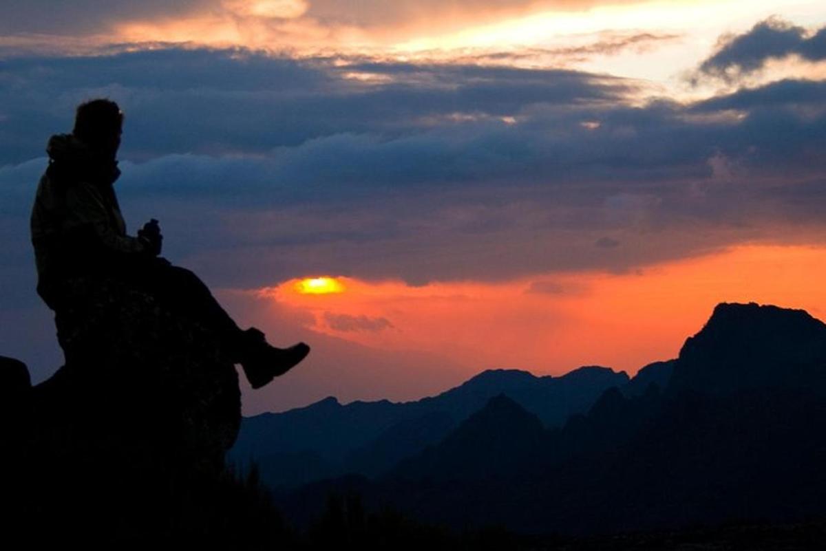en person som sitter på toppen av et fjell ved solnedgang