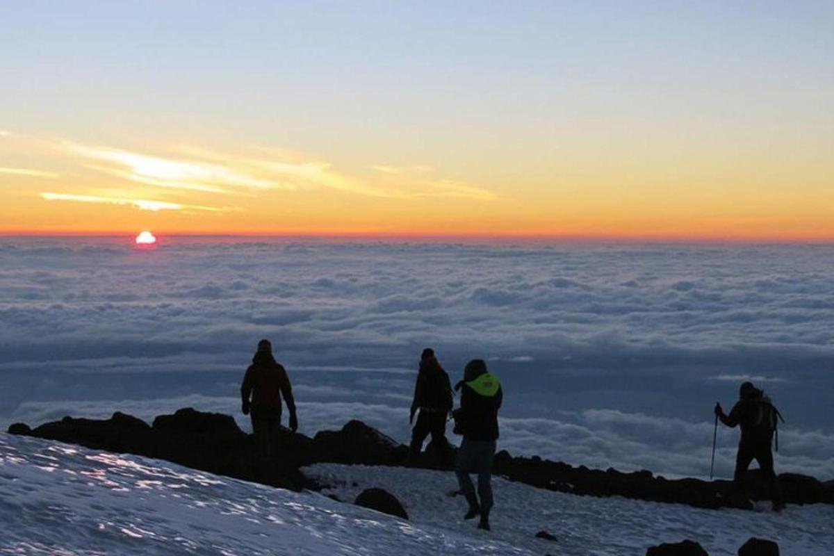 sekumpulan orang berdiri di atas gunung pada waktu matahari terbenam