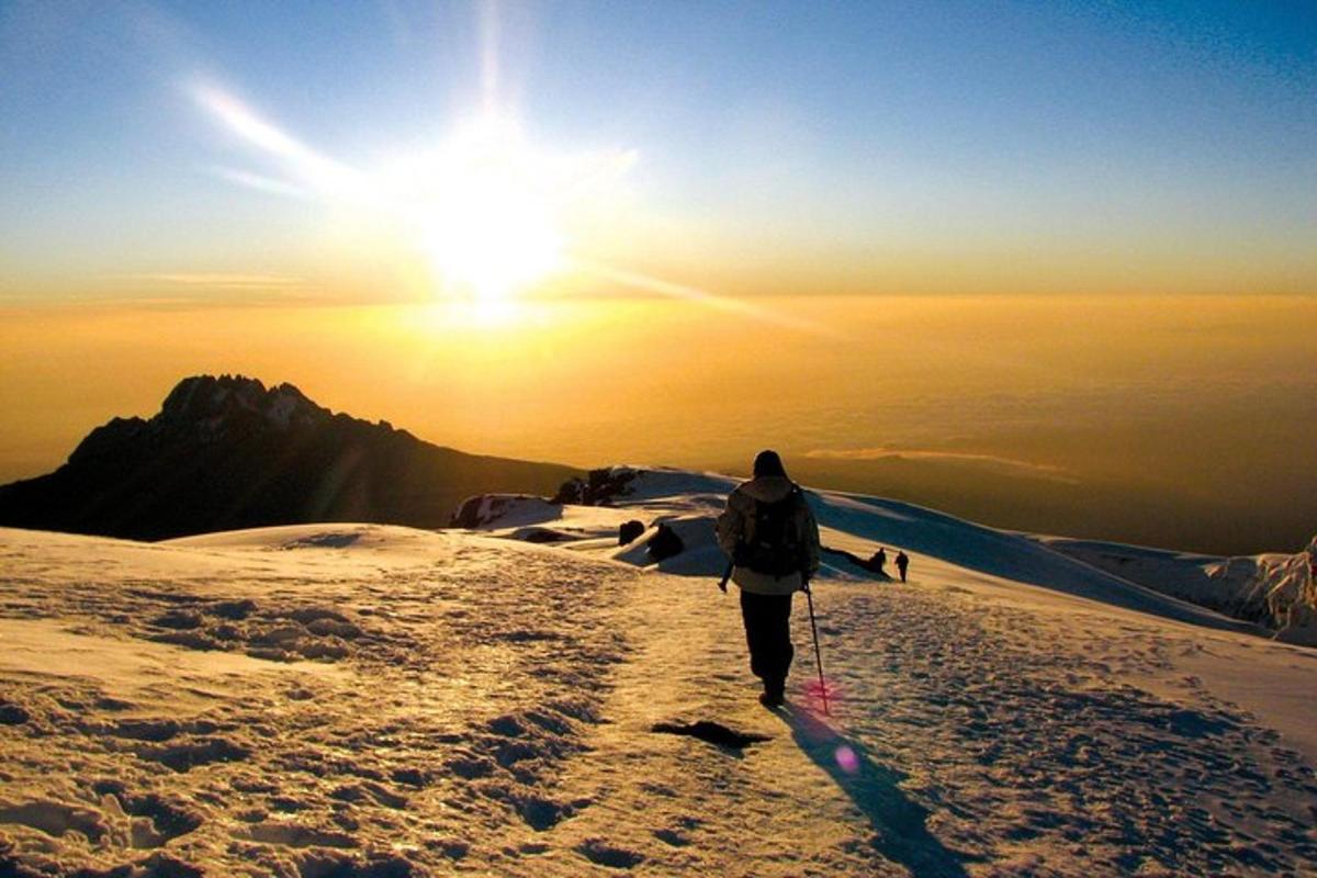seseorang berjalan mendaki gunung yang dilitupi salji pada waktu matahari terbenam