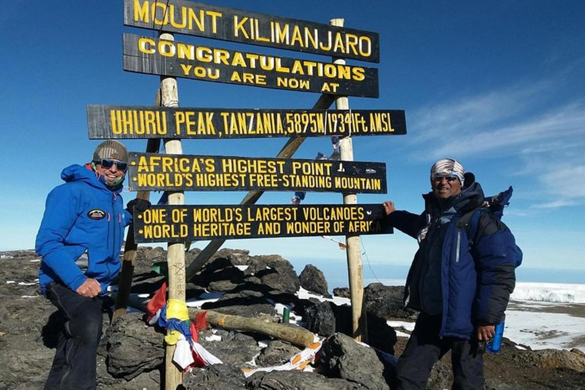 dua lelaki berdiri di sebelah papan tanda di puncak gunung