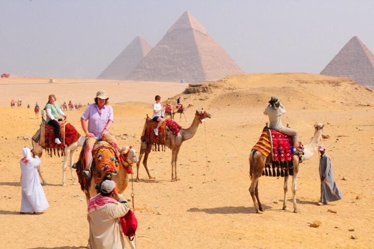 Skupina lidí jedoucích na velbloudech před pyramidami
