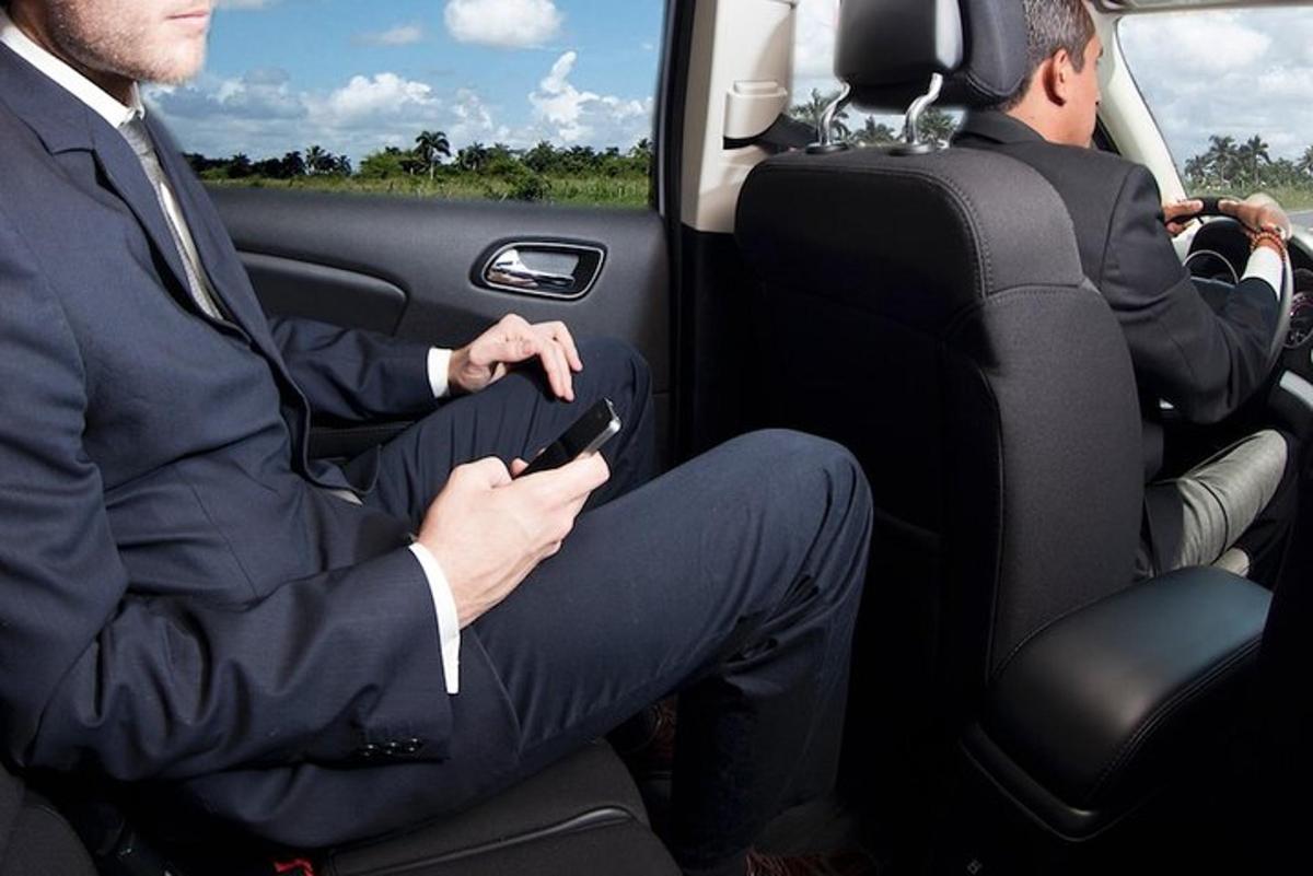 dva muži sedící v zadní části auta a dívající se do svých mobilních telefonů
