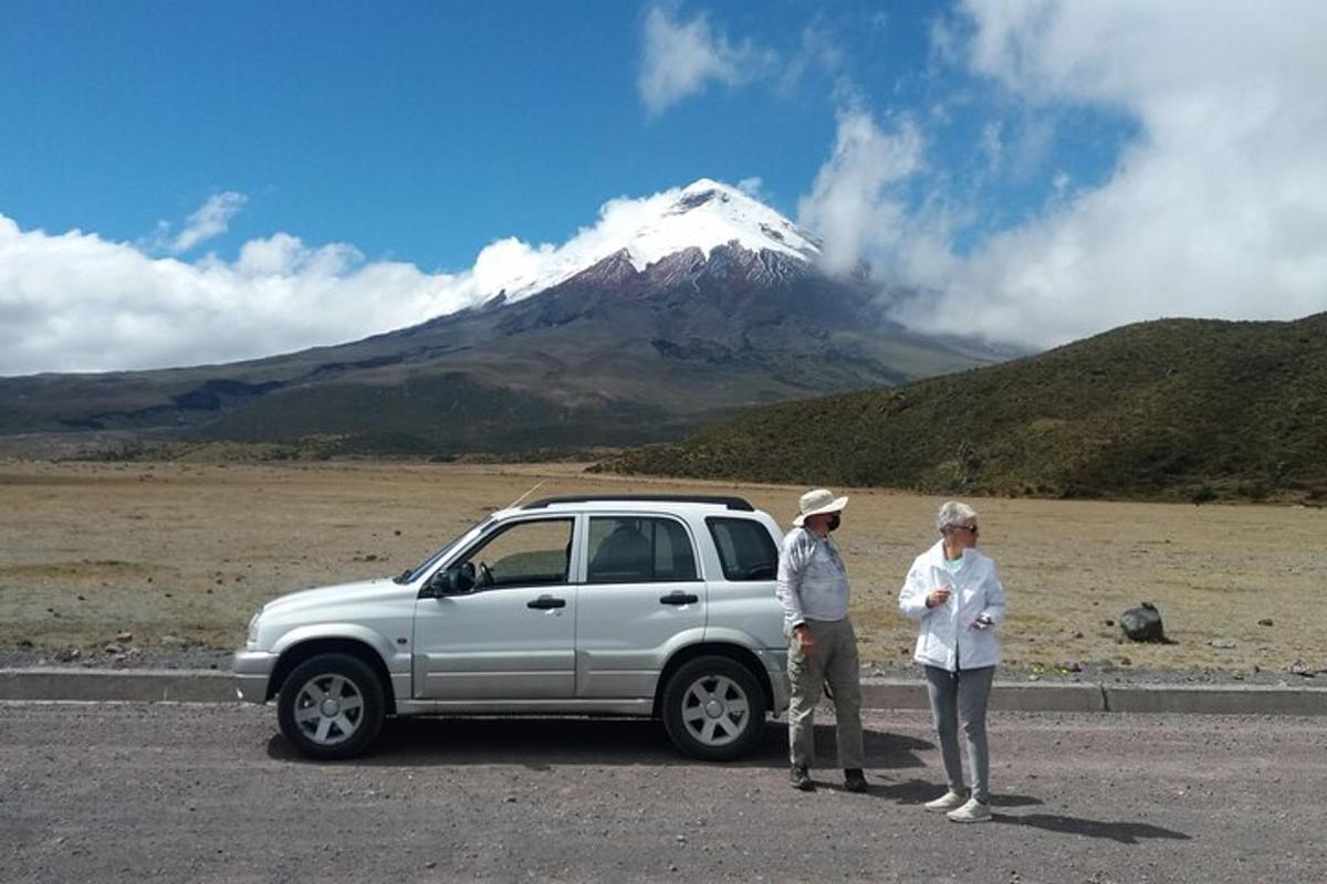 two people standing next to a car in front of a mountain