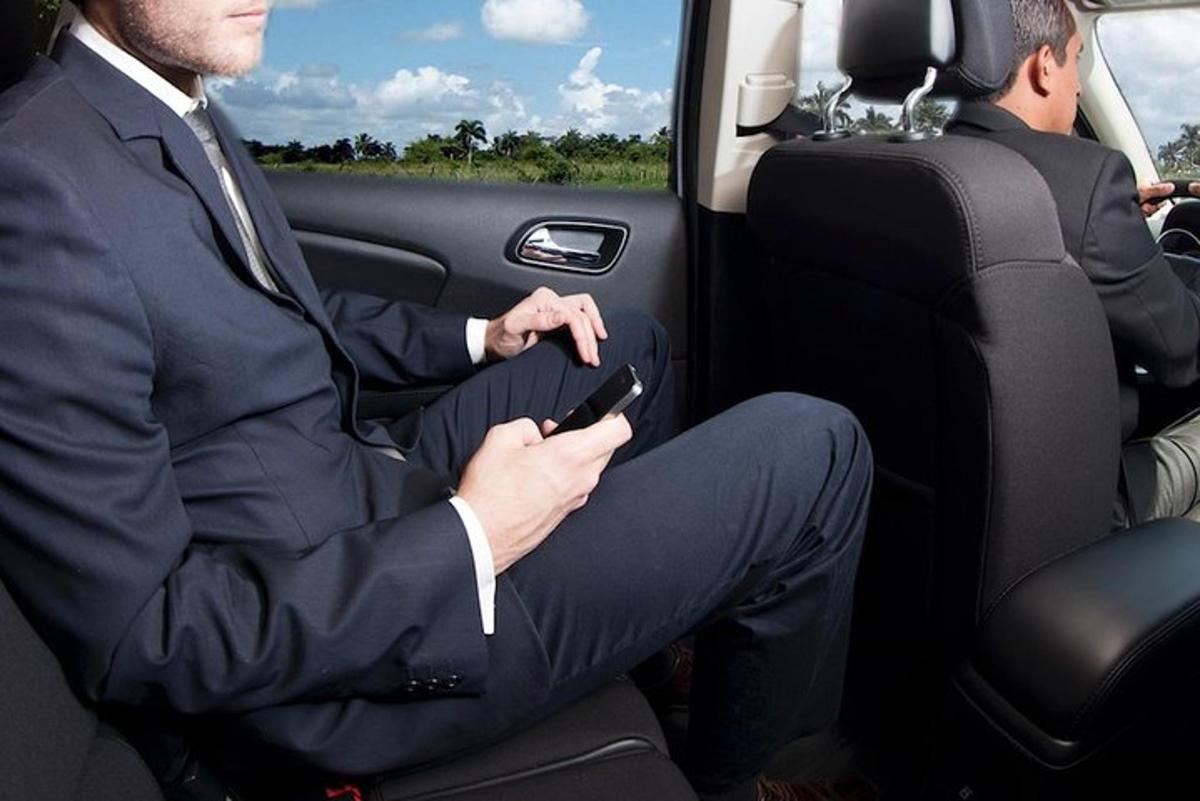 Egy öltönyös férfi ül egy autóban egy mobiltelefonnal