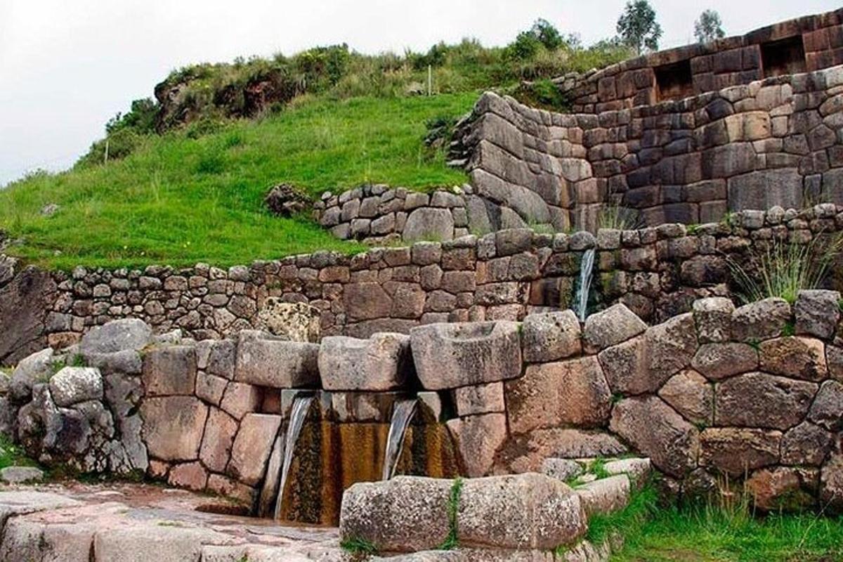 un mur de pedra amb una cascada davant d'un turó