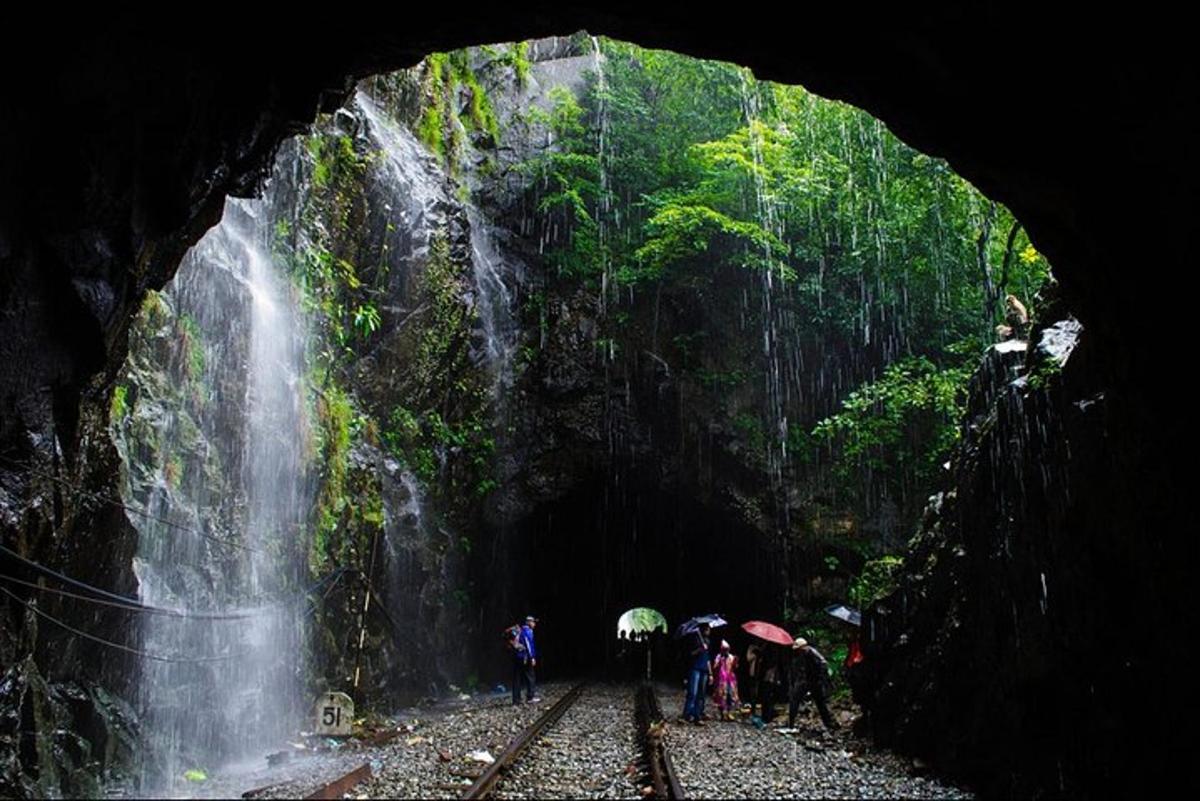 um grupo de pessoas com guarda-chuvas em pé em frente a uma cachoeira