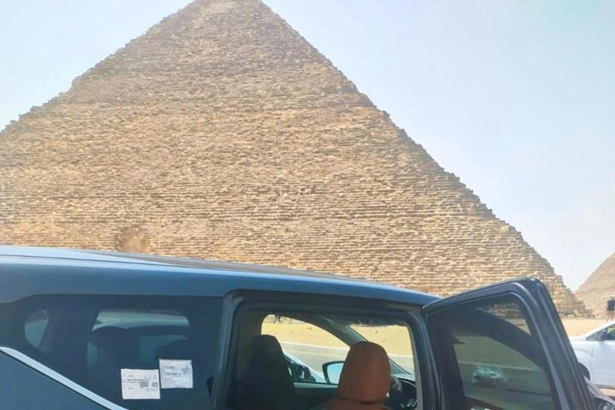 osoba vystrkující ruku z auta před pyramidou
