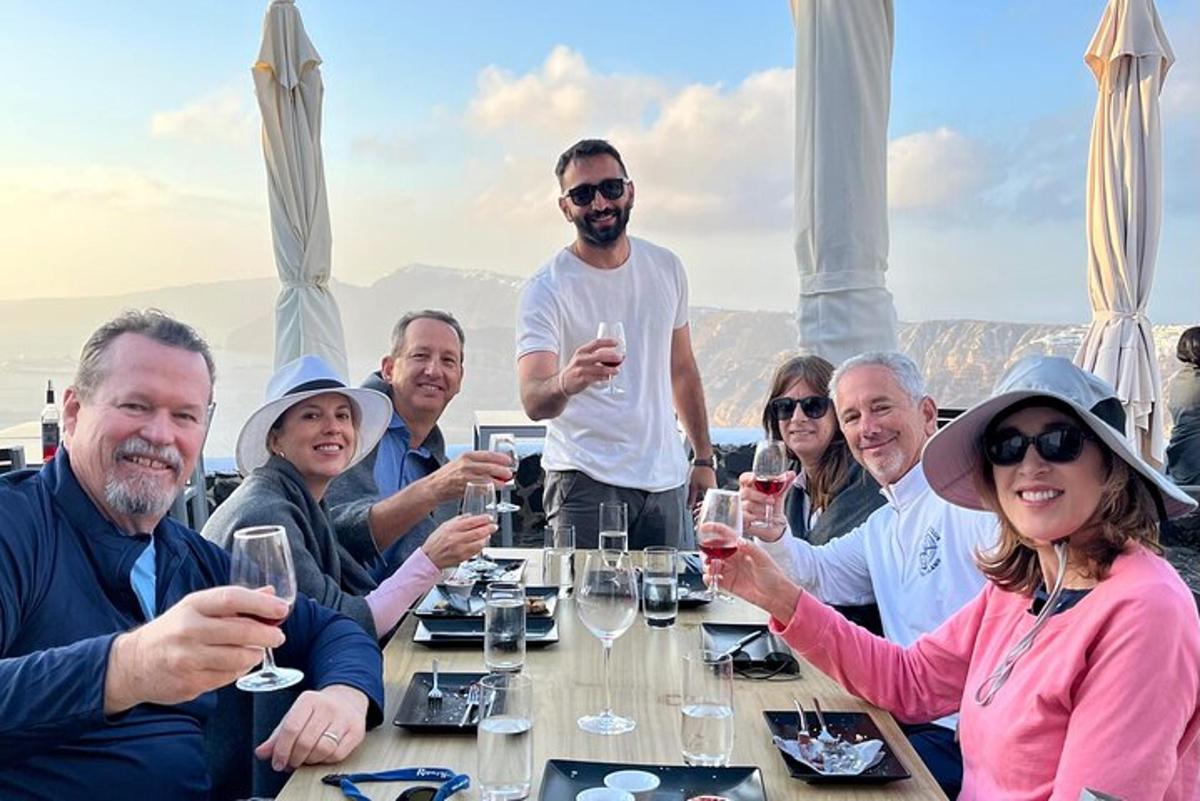 cilvēku grupa sēž pie galda un dzer vīnu