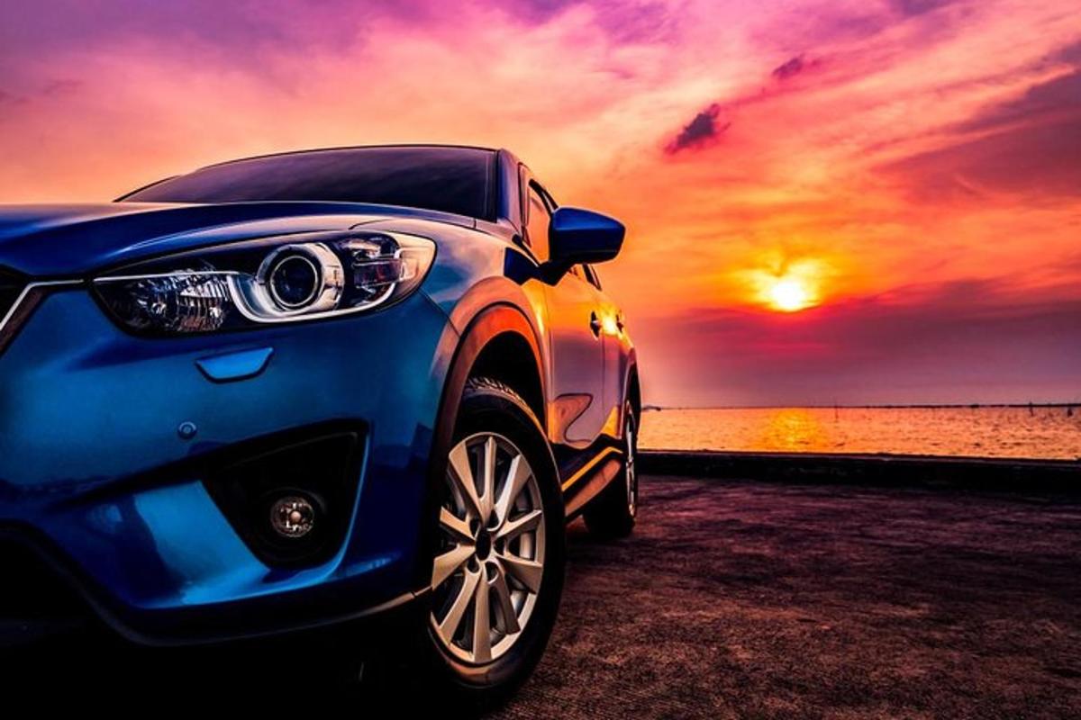 a blue car parked next to the ocean with a sunset