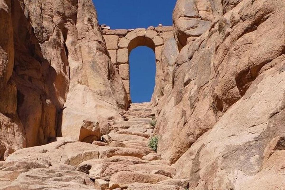 a stone path in a canyon with an arch in the background