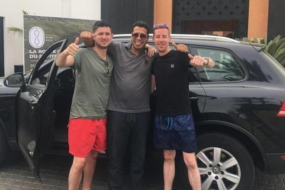 tre menn står foran en bil
