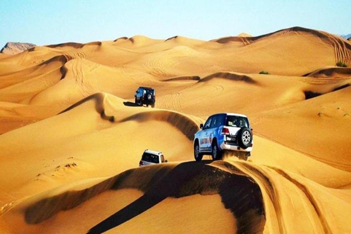 tre camion che guidano sulle dune di sabbia nel deserto
