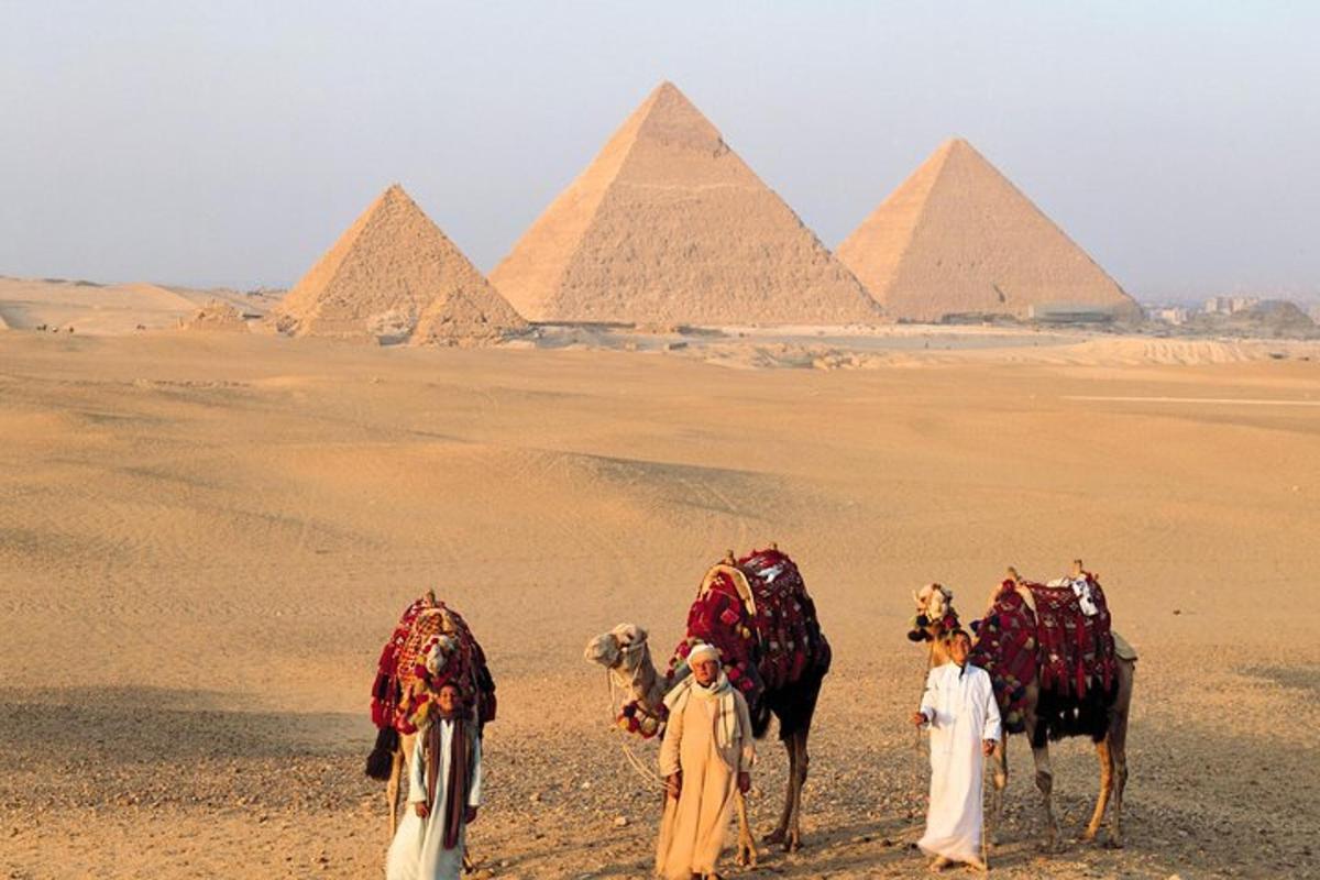 skupina ľudí s ťavami pred pyramídami