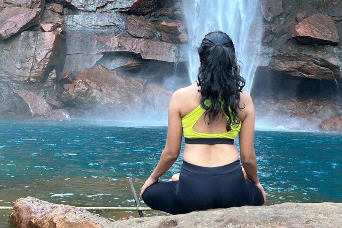 a woman sitting on a rock in front of a waterfall