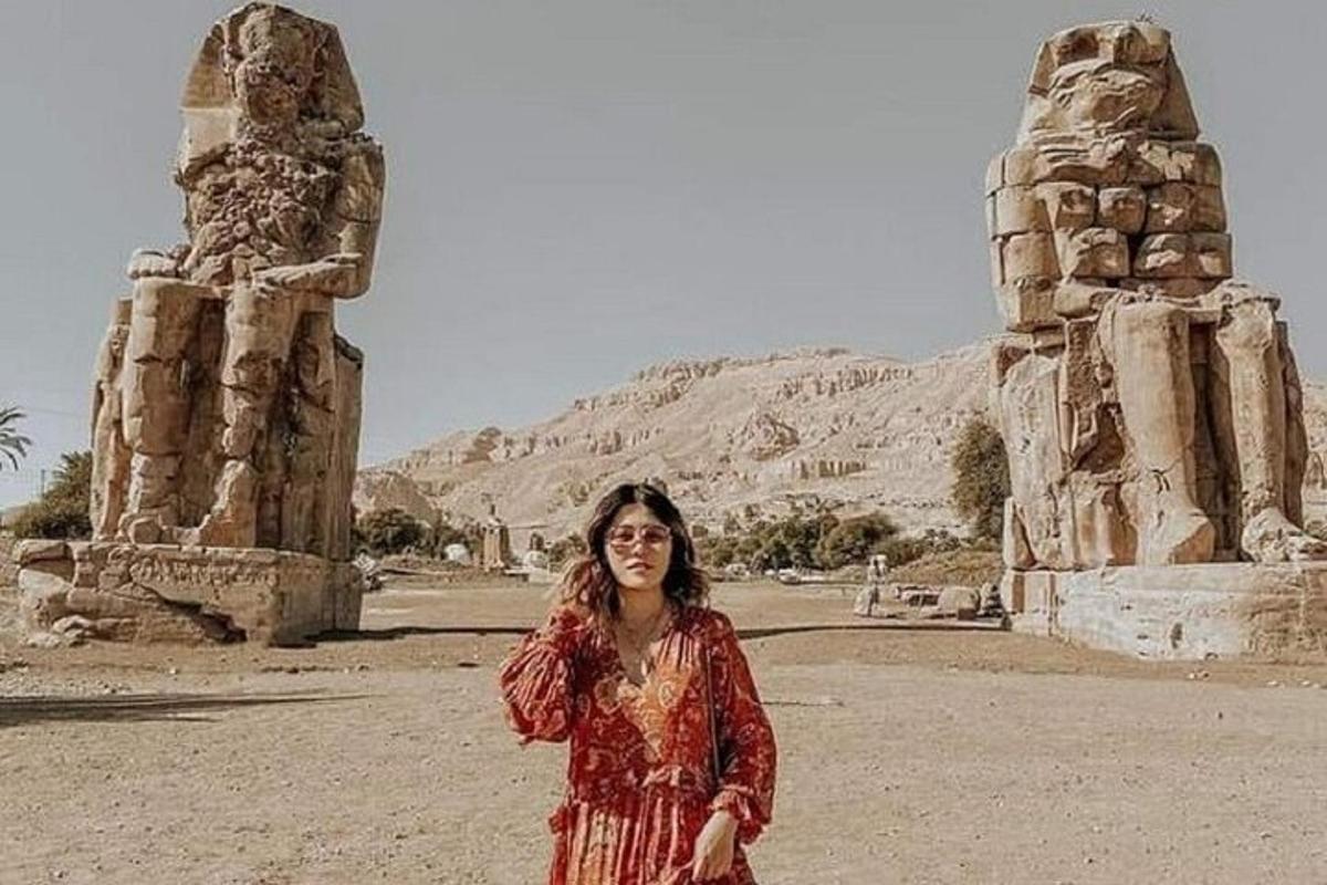 una donna in un vestito rosso in piedi davanti alle rovine