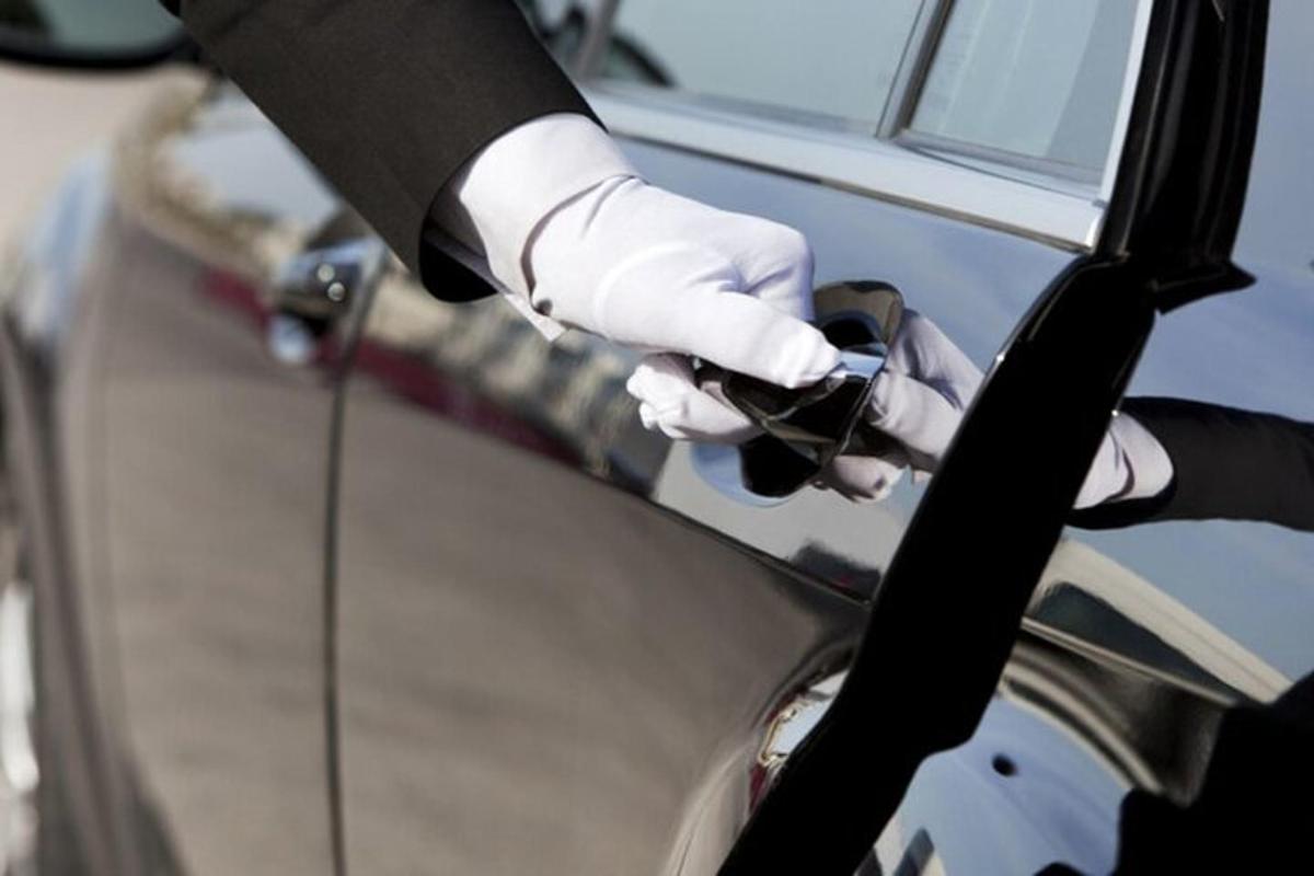eine Person in Anzug und Handschuhen, die eine Autotür hält