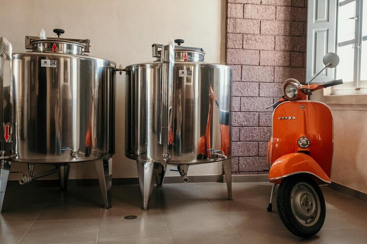 Un scooter naranja estacionado junto a dos tanques de fermentación