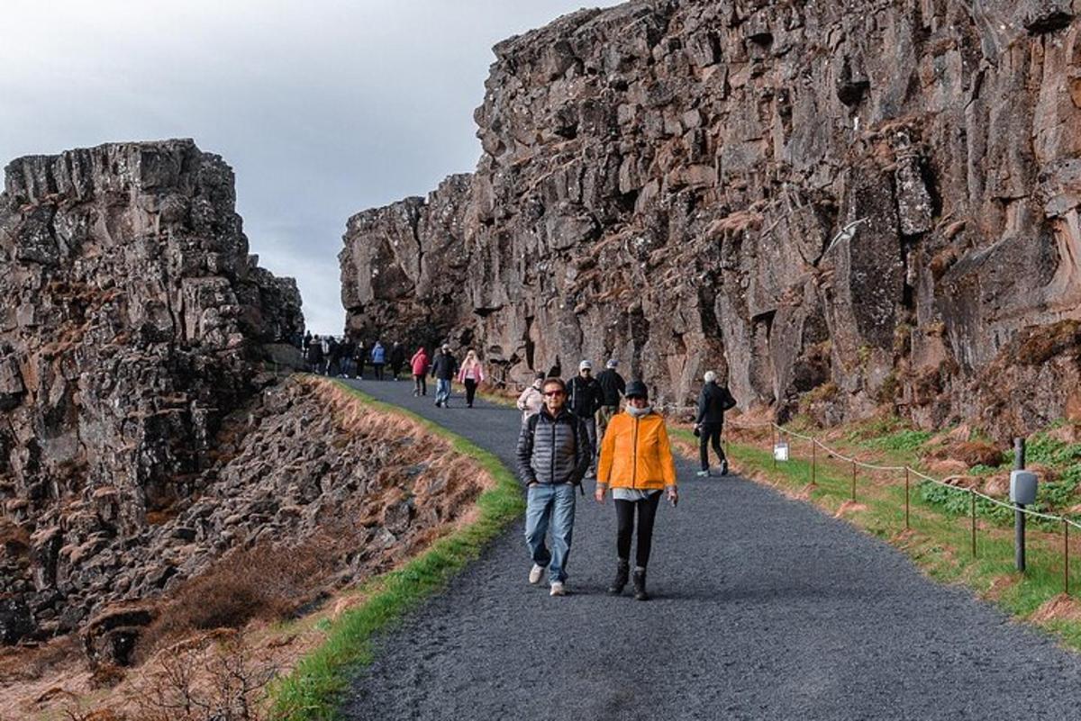people walking down a road next to a rock wall