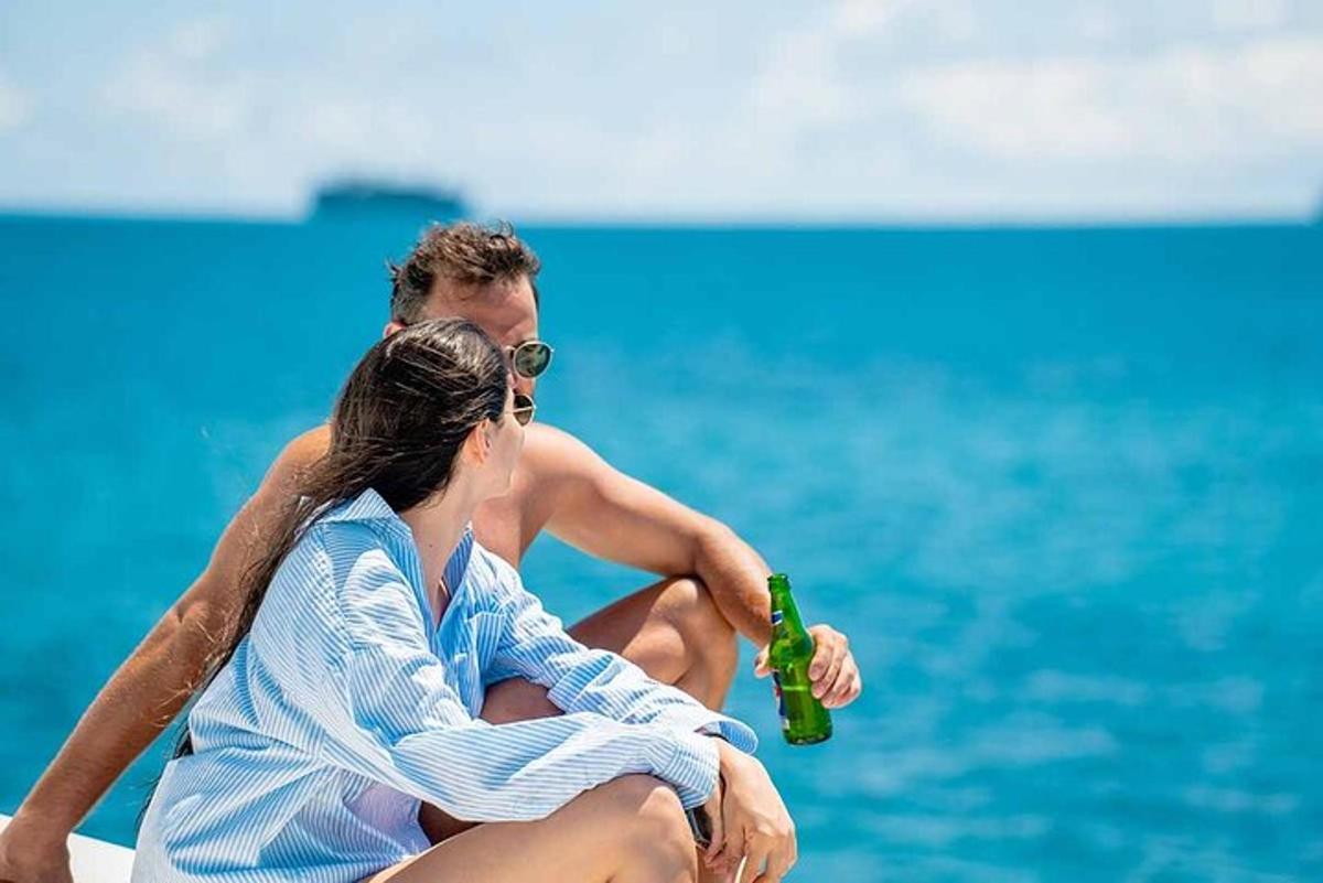 a man and a woman sitting on the beach with a beer