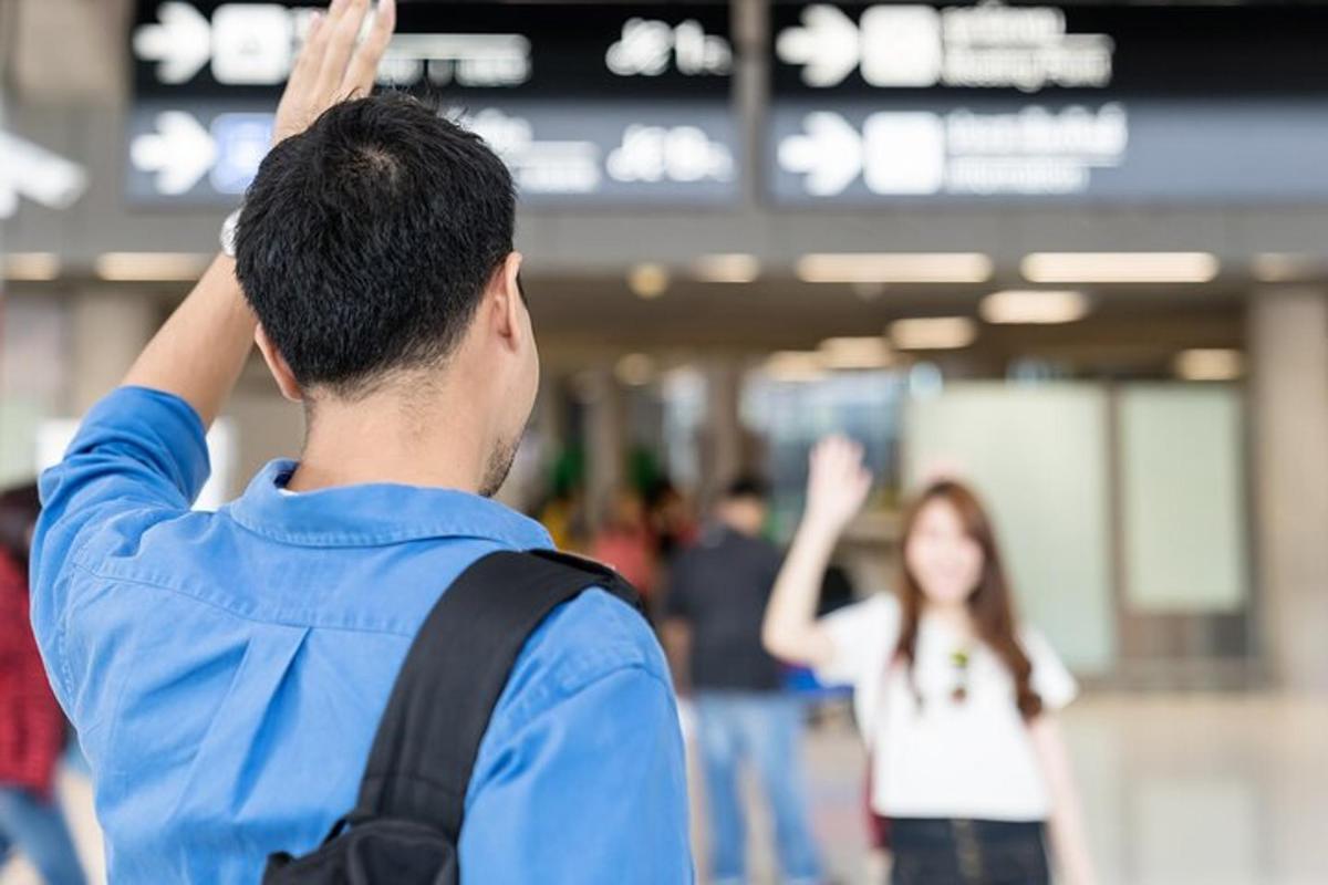 muž s batohem salutující ženě na letišti