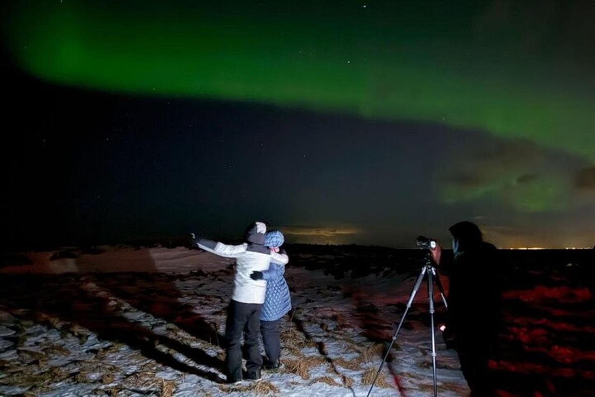 two people standing on a mountain looking at the northern lights