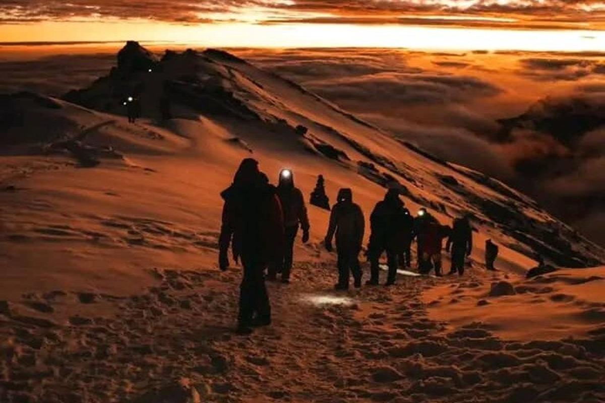 un grup de oameni care urcă un munte la apus