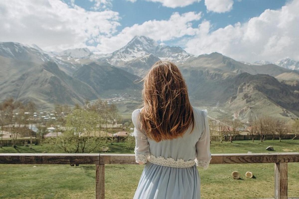 Una mujer parada en una valla mirando las montañas