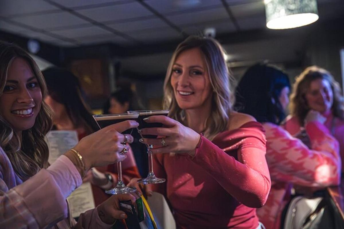two women holding wine glasses and looking at a cell phone