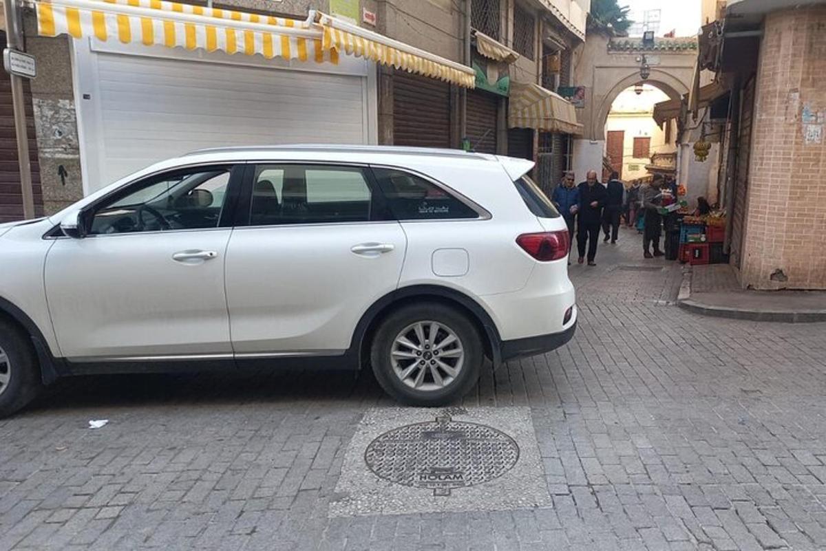 bel avto parkiran na ulici poleg moške luknje