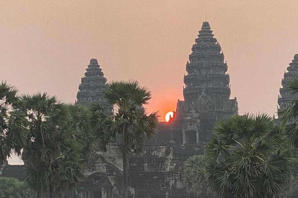 Una puesta de sol detrás de tres torres con palmeras al frente.