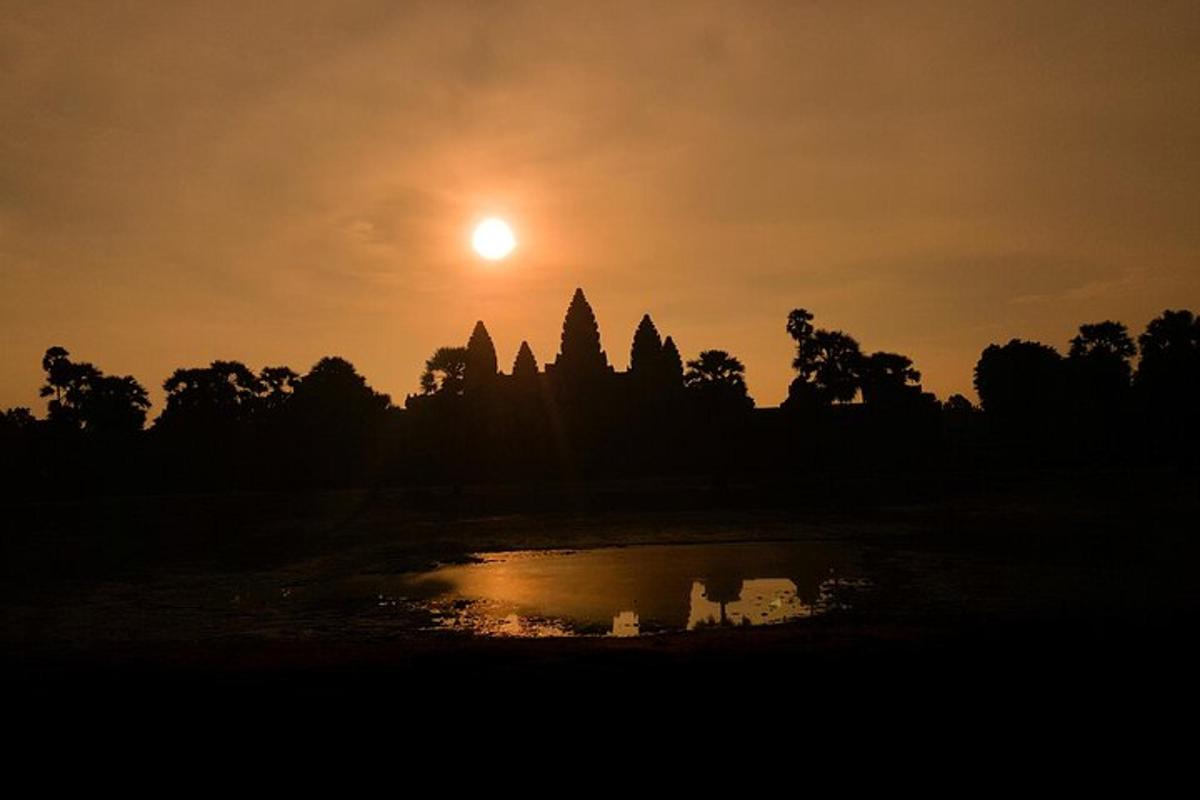 Una puesta de sol frente a un templo con un estanque.