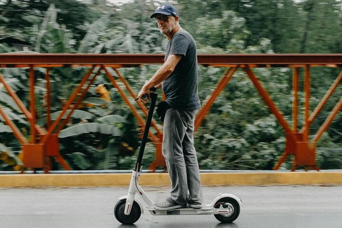 Starší muž jedoucí po ulici na skútru