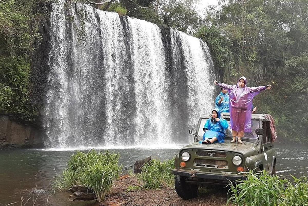 a man and woman standing on the back of a truck in front of a waterfall
