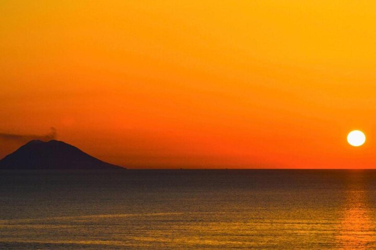 an orange sunset over the ocean with a mountain